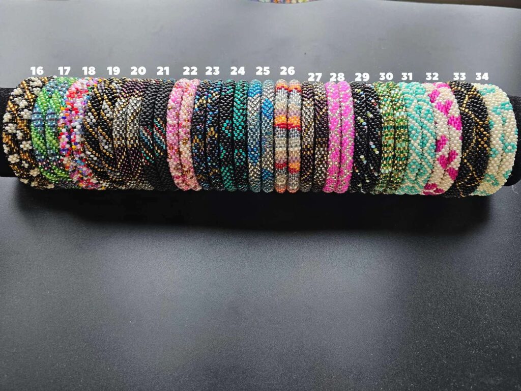 Close-up of handmade beaded bracelets, numbered 16 to 34, featuring colorful glass bead patterns on a black display roll.